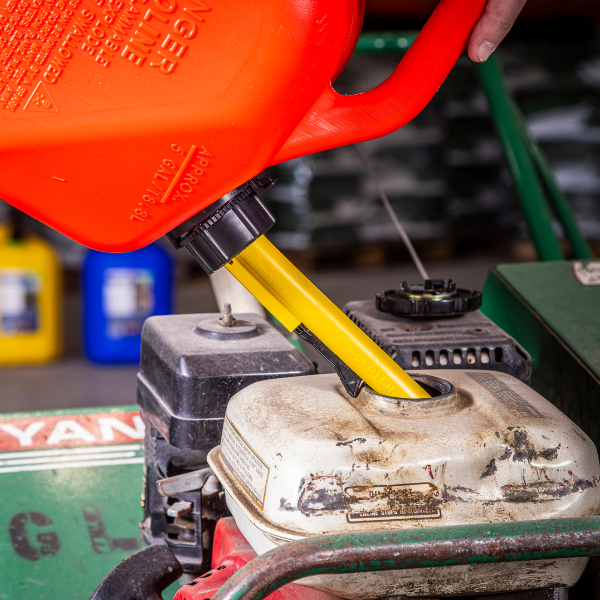 Red gas can with yellow spout filling a well-used lawn mower.